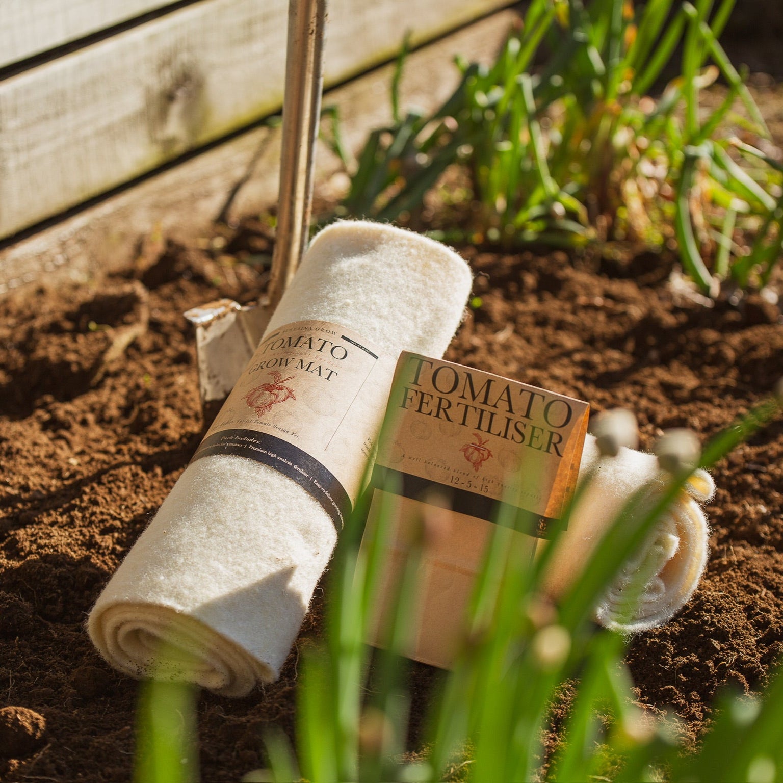 Roll of tomato mulch and fertilizer on garden soil with wooden fence in background